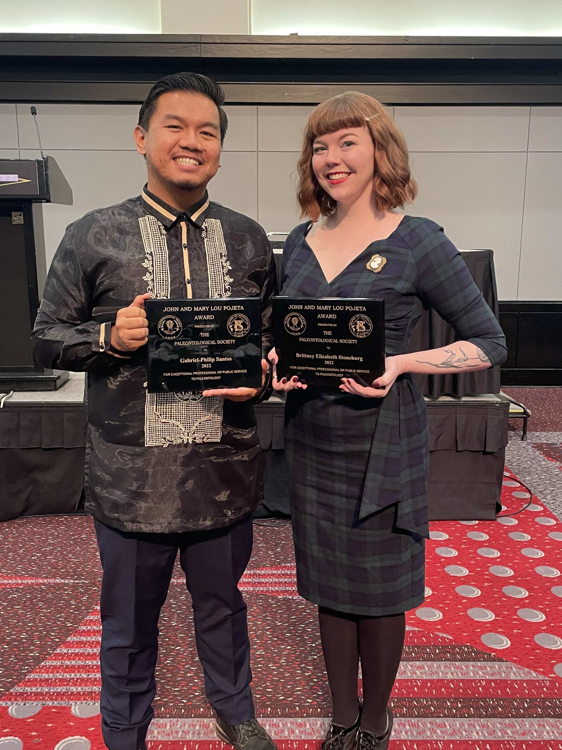 A filipino man and white woman pose next to each other holding award plaques.