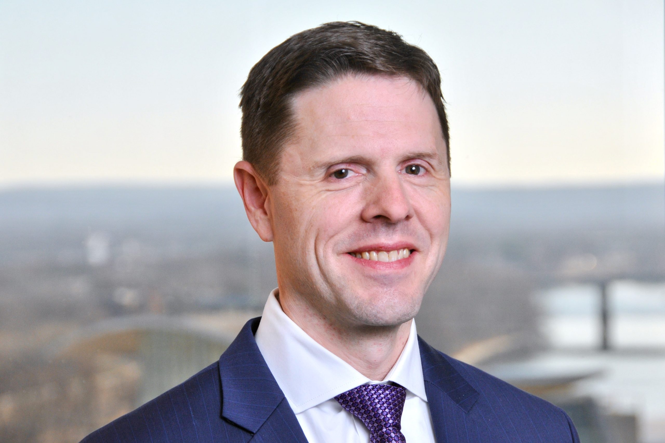 A professional headshot of Tyler Hokanson wearing a dark blue suit