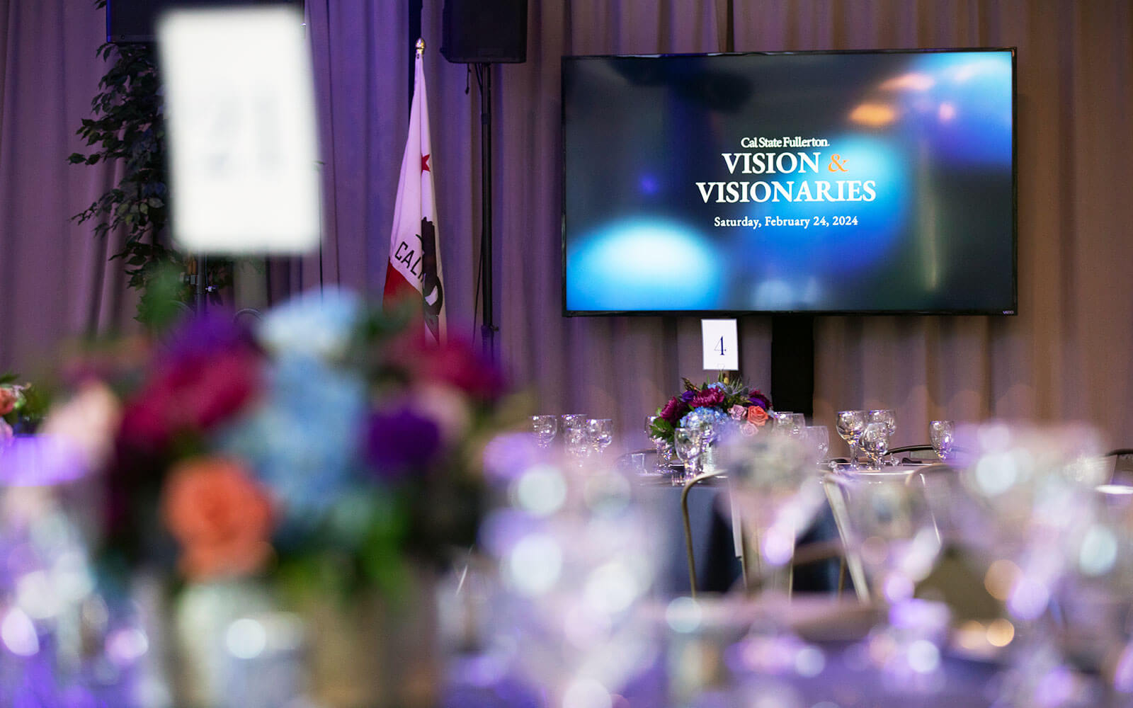 Vision & Visionaries event set up, tables and flowers with digital display of event logo